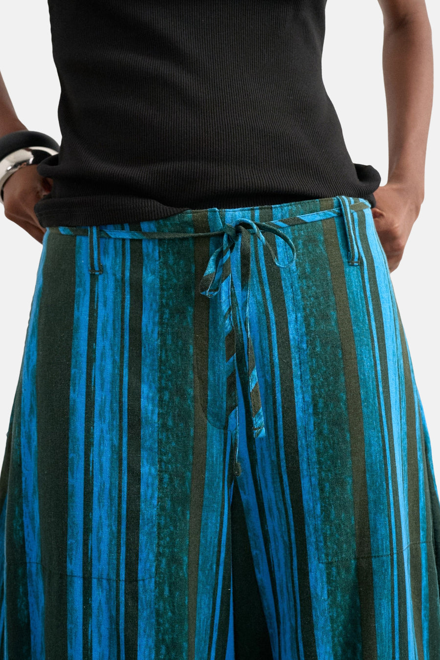 Pantalon rayé bleu de TOPSHOP avec cordon de serrage et rayures vert foncé, porté avec un haut côtelé noir et un bracelet argenté.