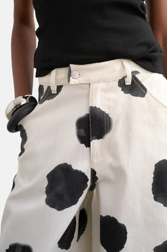 Ecru broek van TOPSHOP, met een zwart vlekkenpatroon en zilveren armband om de pols.
