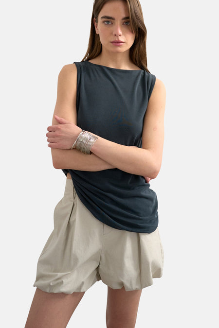 Shorts écru de TOPSHOP avec plis, portés par une personne qui remonte un haut bleu foncé et porte des bracelets argentés.