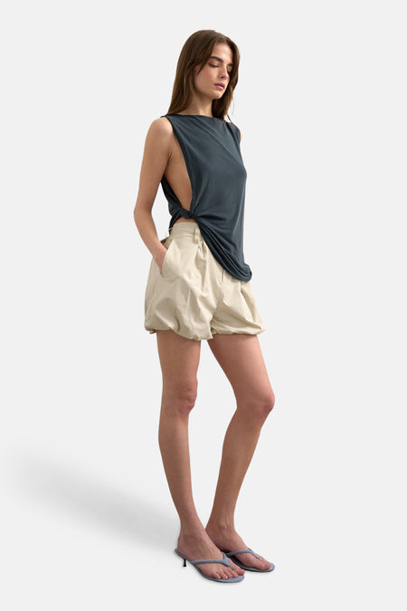 Short écru de TOPSHOP à taille haute et coupe volumineuse, porté par un mannequin dans un débardeur gris foncé et des tongs à talons bleu clair.