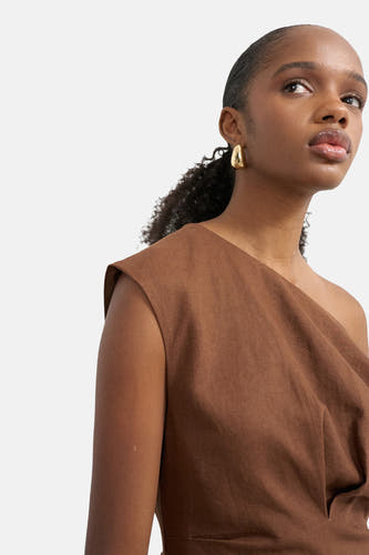 Bruine asymmetrische jurk van TOPSHOP, van getextureerde stof, gedragen door een vrouw met gouden oorbellen.