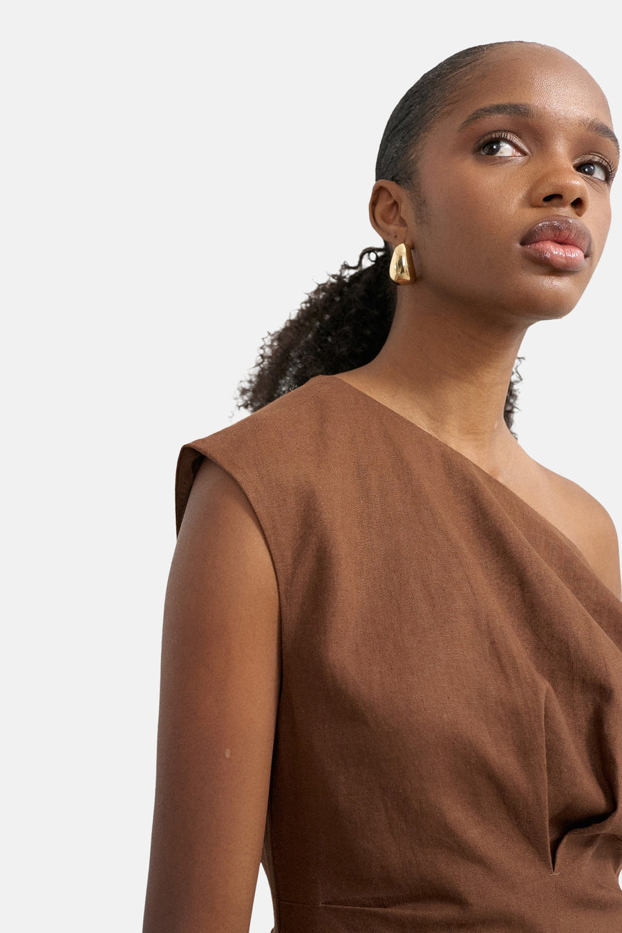 Bruine asymmetrische jurk van TOPSHOP, van getextureerde stof, gedragen door een vrouw met gouden oorbellen.