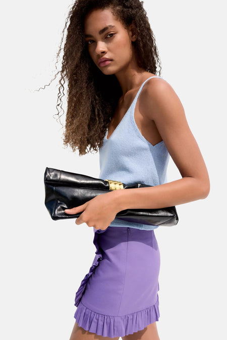 Blauwe mouwloze gilet van MANGO, gebreid met V-hals, gedragen met paarse rok en zwarte clutch, zijprofiel.