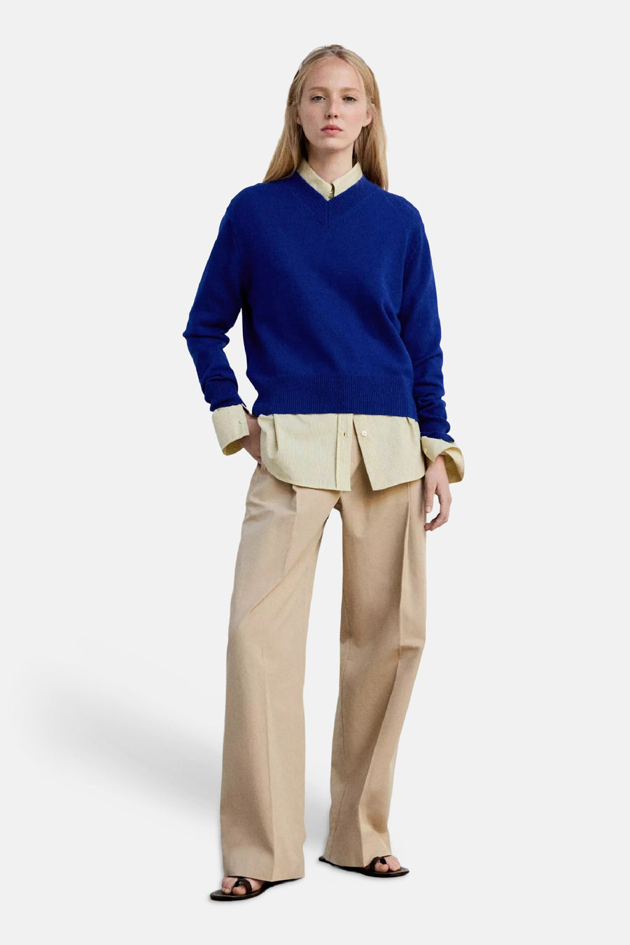 Blauwe V-hals trui van MANGO, gebreid met ribboorden, gedragen over een crèmekleurige blouse en beige broek, front view.