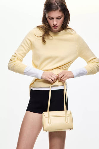 Gele ronde hals trui van MANGO, gebreid met ceintuurdetail, gedragen over witte blouse en zwarte shorts, lifestyle shot