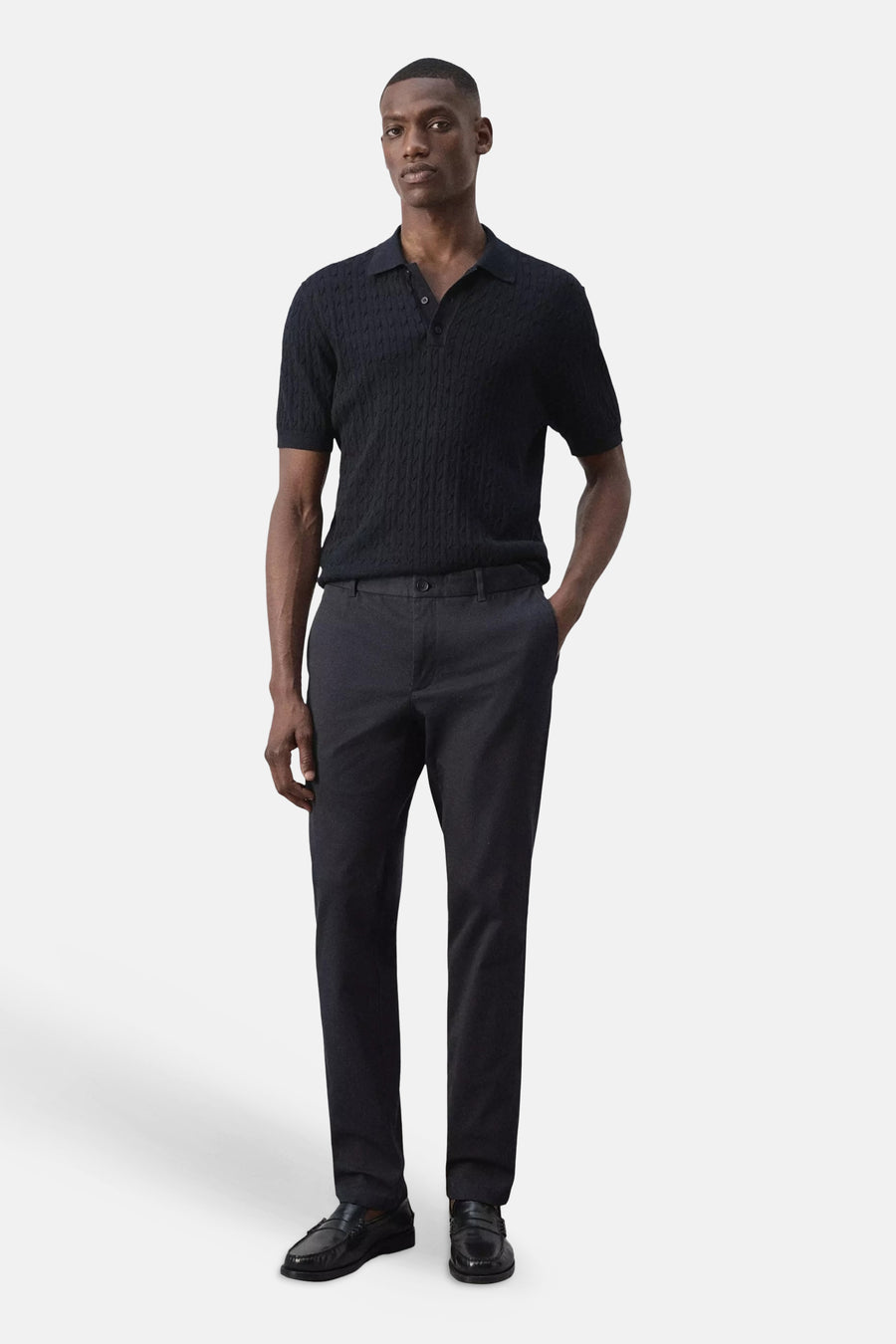 Blauwe chino's van MANGO, strakke pasvorm, gedragen met donkere gebreide polo en zwarte loafers, front view.
