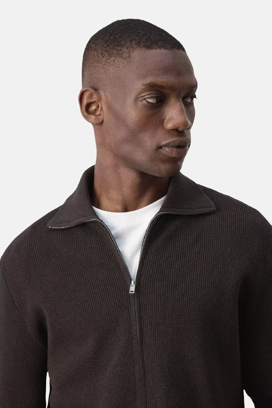Bruine ribbelpull met rolkraag van MANGO, voorzien van rits en gedragen over een wit T-shirt, close-up vooraanzicht