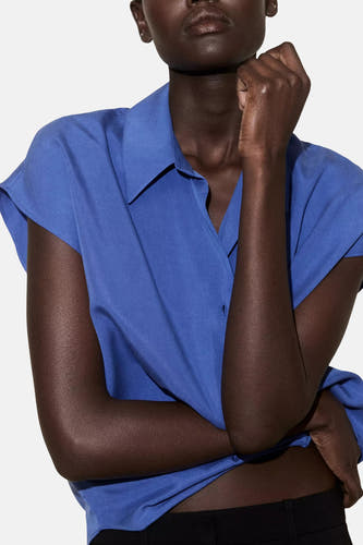 Blauw mouwloos overhemd van MANGO, gekreukt stof, V-hals, model draagt met zwarte broek, close-up voorzijde