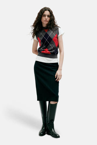 Multicolor argyle gilet van MANGO, gedragen over een witte t-shirt met donkere plooikous en zwarte laarzen, front view.