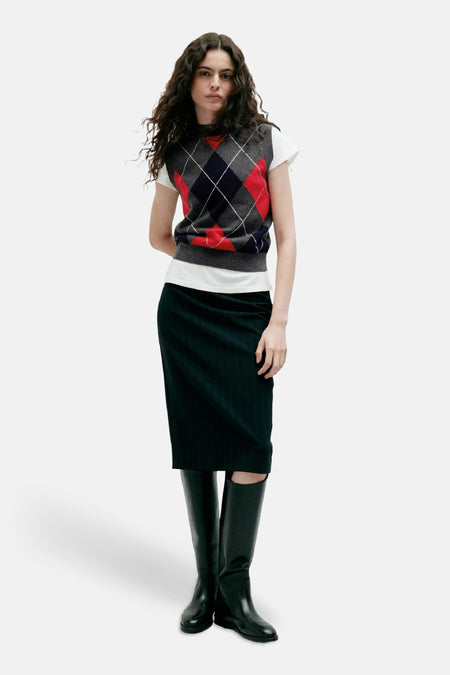 Multicolor argyle gilet van MANGO, gedragen over een witte t-shirt met donkere plooikous en zwarte laarzen, front view.