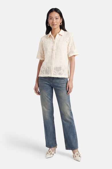 Chemisier beige à manches courtes de Terra di Siena, avec motif ajouré, porté avec un jean et des escarpins.