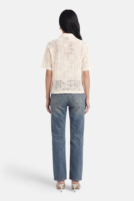 Chemisier beige à manches courtes de Terra di Siena, ajouré à motif floral, vue arrière, porté sur un jean et des talons.