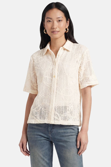 Chemisier beige à manches courtes de Terra di Siena, avec motif ajouré, porté sur un jean.