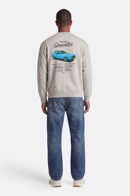 Grijze sweater van Levi's® met een blauwe AMC Gremlin auto en tekst op de rug, gedragen door een man met blauwe spijkerbroek en sneakers.