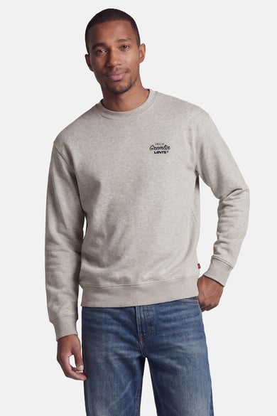 Pull gris à col rond de Levi's® avec impression du logo et étiquette rouge sur l'ourlet, porté par un homme sur un jean bleu.