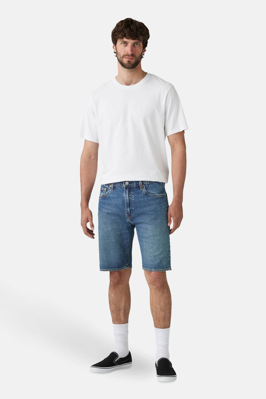 Man in wit T-shirt en denim shorts met zwarte slip-on schoenen.