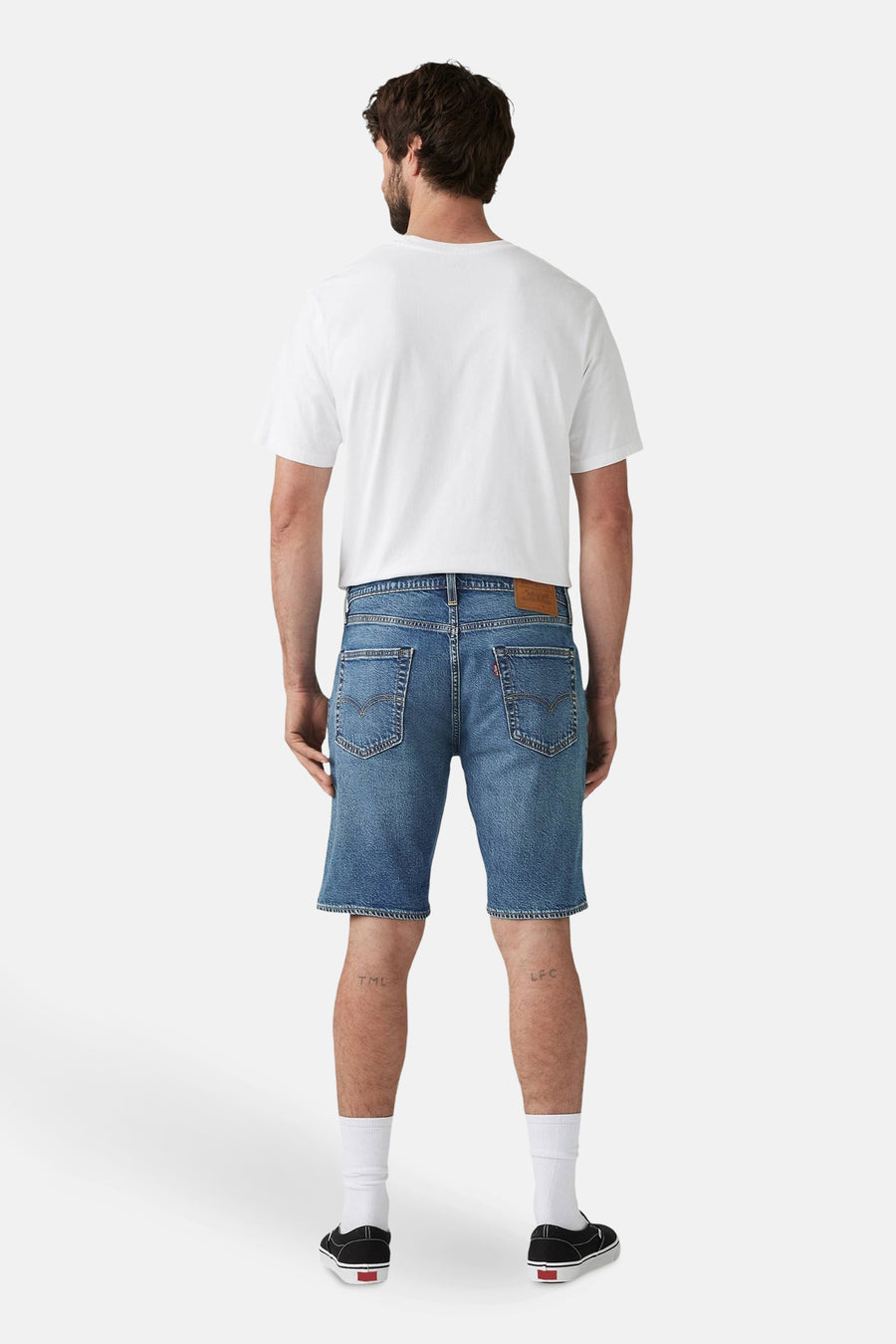 Man van achter, wit t-shirt, blauwe Levi's shorts, witte sokken, zwarte Vans schoenen.