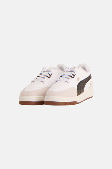 Witte sneakers van PUMA met zwarte streep en crèmekleurige suède details, op een witte zool met bruine onderkant.
