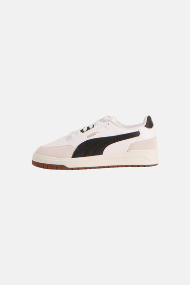 Witte sneakers van PUMA met zwarte accentstreep en bruine zool, in zijaanzicht.