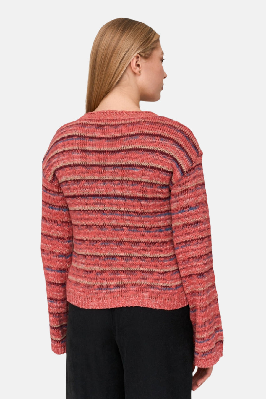 Een vrouw van achteren gezien, ze draagt een gestreepte roze, blauwe en bruine trui en een zwarte broek.