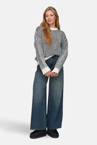 Vrouw met gestreepte trui, wijde jeans en zwarte schoenen.
