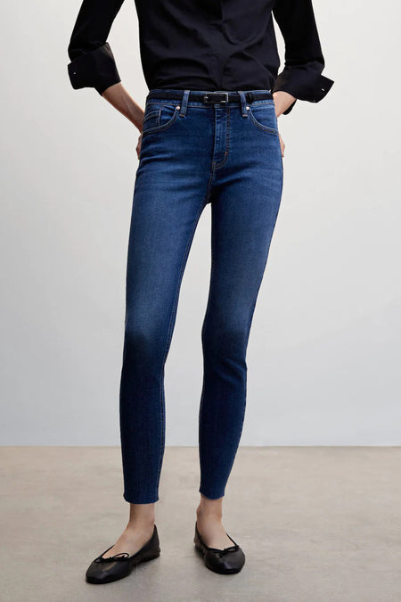 Jeans skinny taille haute en denim bleu moyen de MANGO, portées avec un chemisier noir, une ceinture noire et des ballerines.