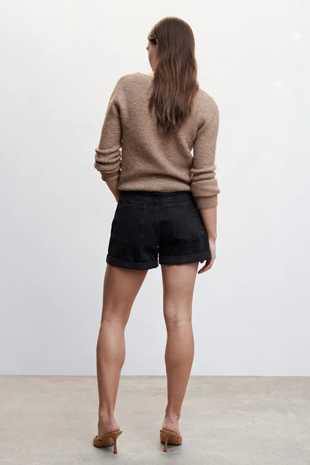 Zwarte 5-pocket shorts van MANGO, achterzijde, met opgerolde pijpen en beige trui, model in hoge hakken
