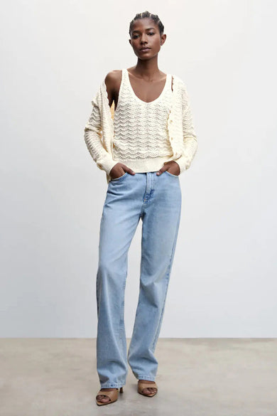 Beige gebreide tanktop van MANGO, met diep V-hals en openwork patroon, gedragen onder een crèmekleurige cardigan, lichtblauwe jeans en bruine sandalen, front view.