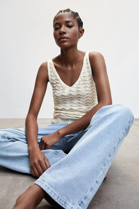 Beige gebreide tanktop met V-hals van MANGO, gedragen met lichtblauwe jeans, zittend in lifestyle pose
