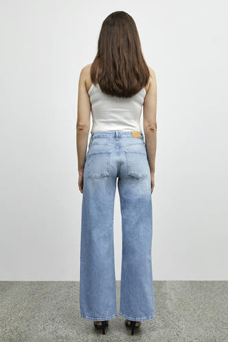 Lichtblauwe wijde jeans van PULZ, achterkant gezien, met een wit hemdje en zwarte hakken.