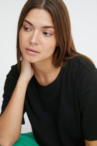Zwart T-shirt met korte mouwen van PULZ, gedragen door een vrouw met een groene broek.
