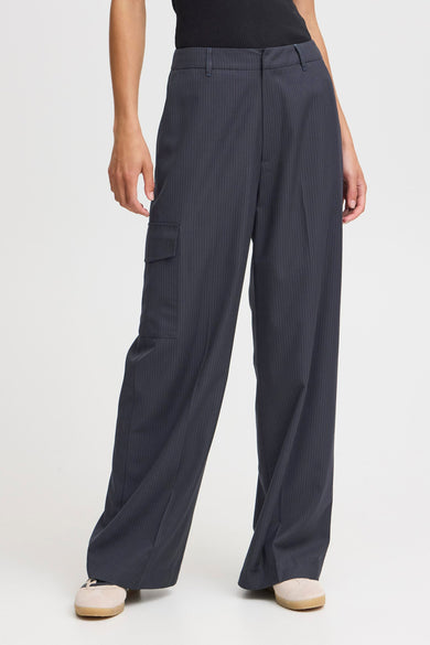 Pantalon bleu de PULZ, avec une rayure blanche et un cargo, porté avec des baskets beige.