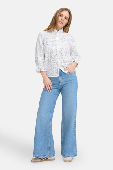 Wijde jeans van mid blue denim van PULZ, gedragen met een geprinte blouse en lage sneakers.
