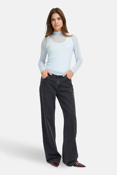 Blauw T-shirt van PULZ, met lange mouwen en een fijne stippenprint, gecombineerd met een wit hemd en zwarte jeans.
