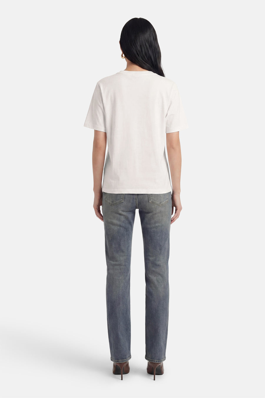 Wit T-shirt met korte mouwen van PULZ, achterkant zichtbaar, gedragen met blauwe jeans en bruine hakken.
