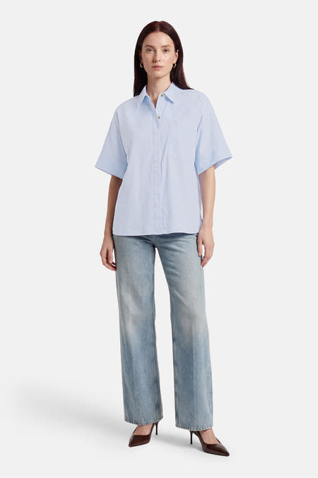 Blauw overhemd met korte mouwen van PULZ, met een borstzak, gedragen met jeans en hakken.