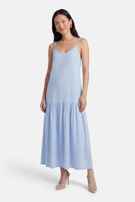 Robe bleue sans manches de PULZ, avec fines bretelles et jupe évasée, portée avec des escarpins beiges.