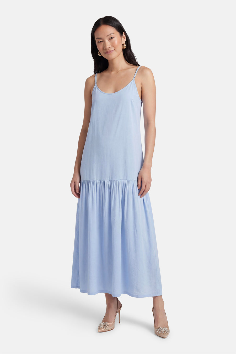Robe bleue sans manches de PULZ, avec fines bretelles et jupe évasée, portée avec des escarpins beiges.
