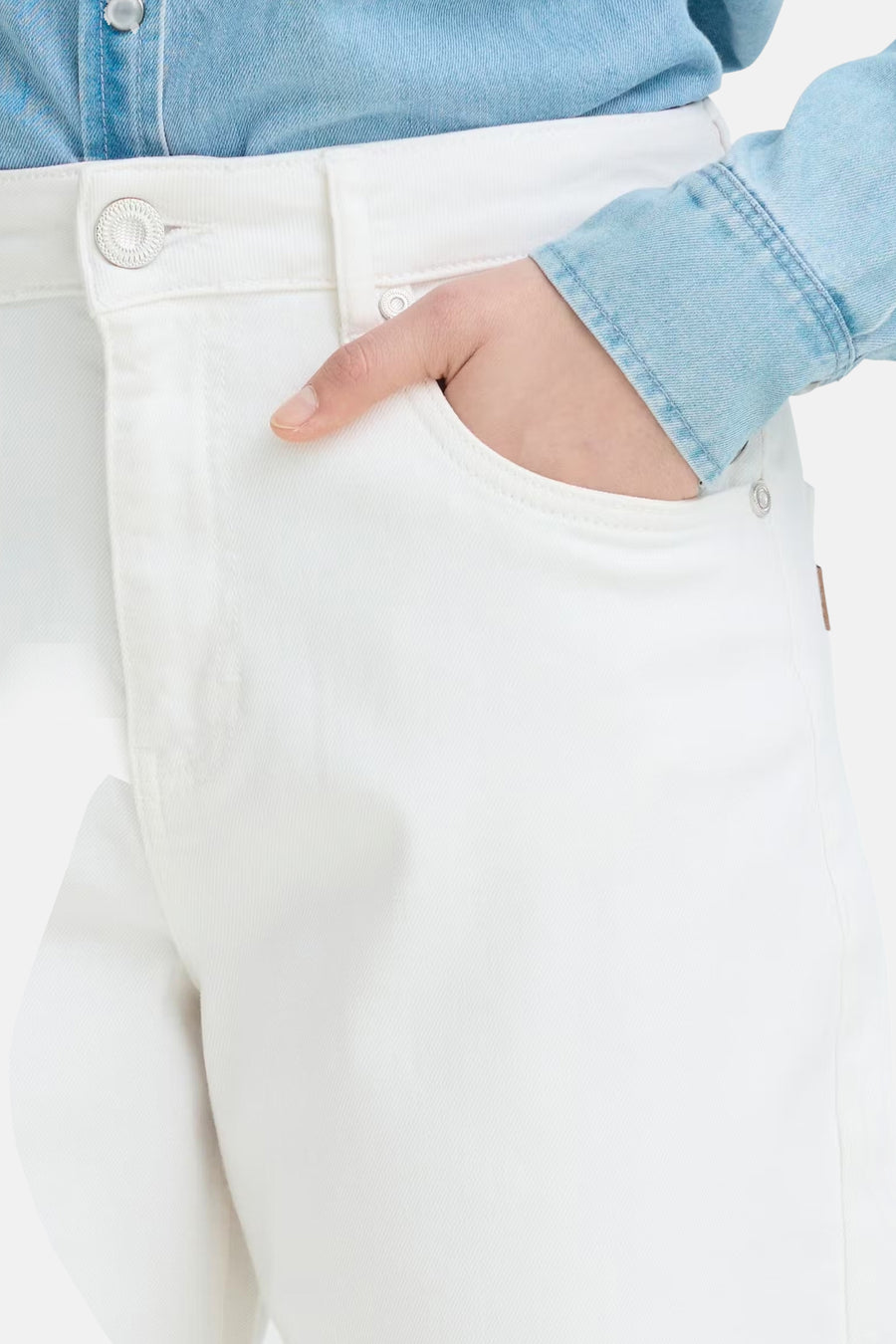 Witte denim jeans van PULZ, detail met een hand in de voorzak, zilveren knoop en een lichtblauw spijker overhemd.