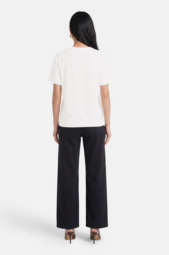 Wit T-shirt van PULZ, van achteren gezien op een model met zwarte wijde broek en bruine hakken.