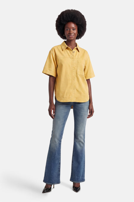 Geel jeanshemd van PULZ met korte mouwen, borstzak, gedragen met blauwe flared jeans en zwarte hakken.