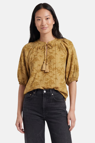 Gele blouse met korte mouwen van PULZ, met bladprint, striksluiting met kwastjes en pofmouwen, gedragen op een zwarte jeans.