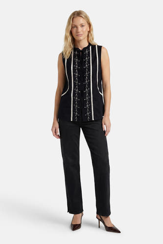 Zwarte mouwloze blouse met witte borduursels en strikdetail van PULZ, gedragen met zwarte broek en bruine hakken, front view