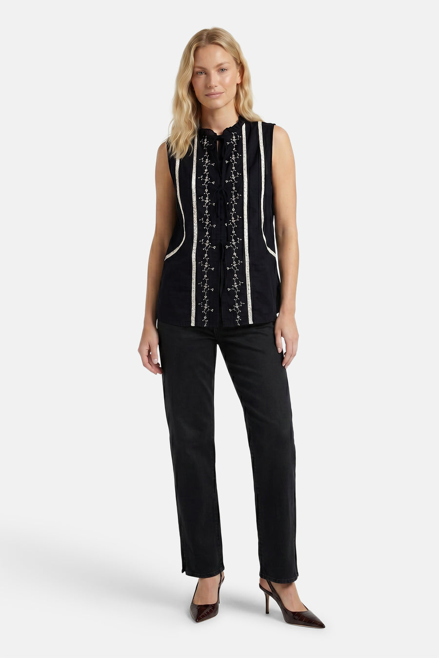 Zwarte mouwloze blouse met witte borduursels en strikdetail van PULZ, gedragen met zwarte broek en bruine hakken, front view