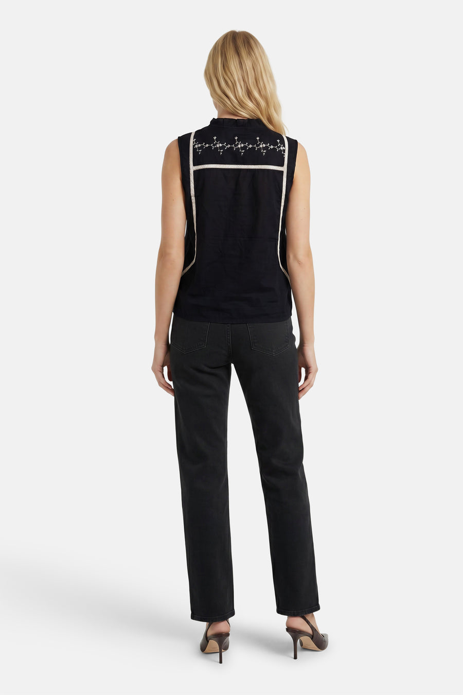 Zwarte mouwloze blouse met witte borduurwerk en ruches aan de rug, van PULZ, getoond van achteren op model in zwarte jeans en hoge hakken.