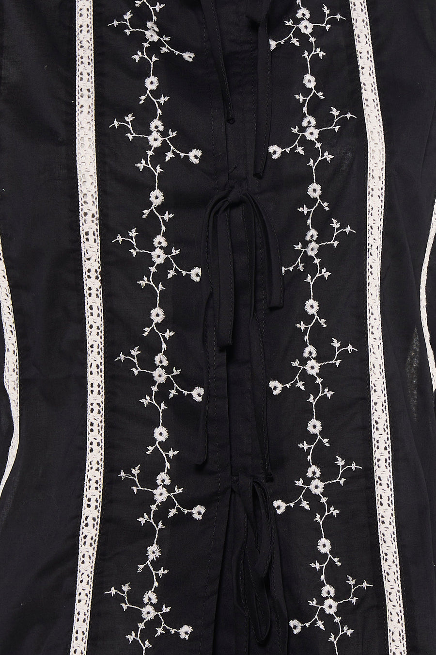 Zwarte mouwloze blouse van PULZ met witte bloemen borduurwerk en kant details, close-up van voorkant