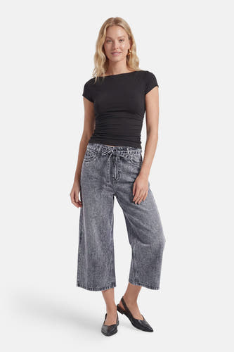 Grijze denim Bermuda van PULZ met hoge taille, wijde pijpen en strikceintuur, gedragen met zwart shirt en zwarte flats.