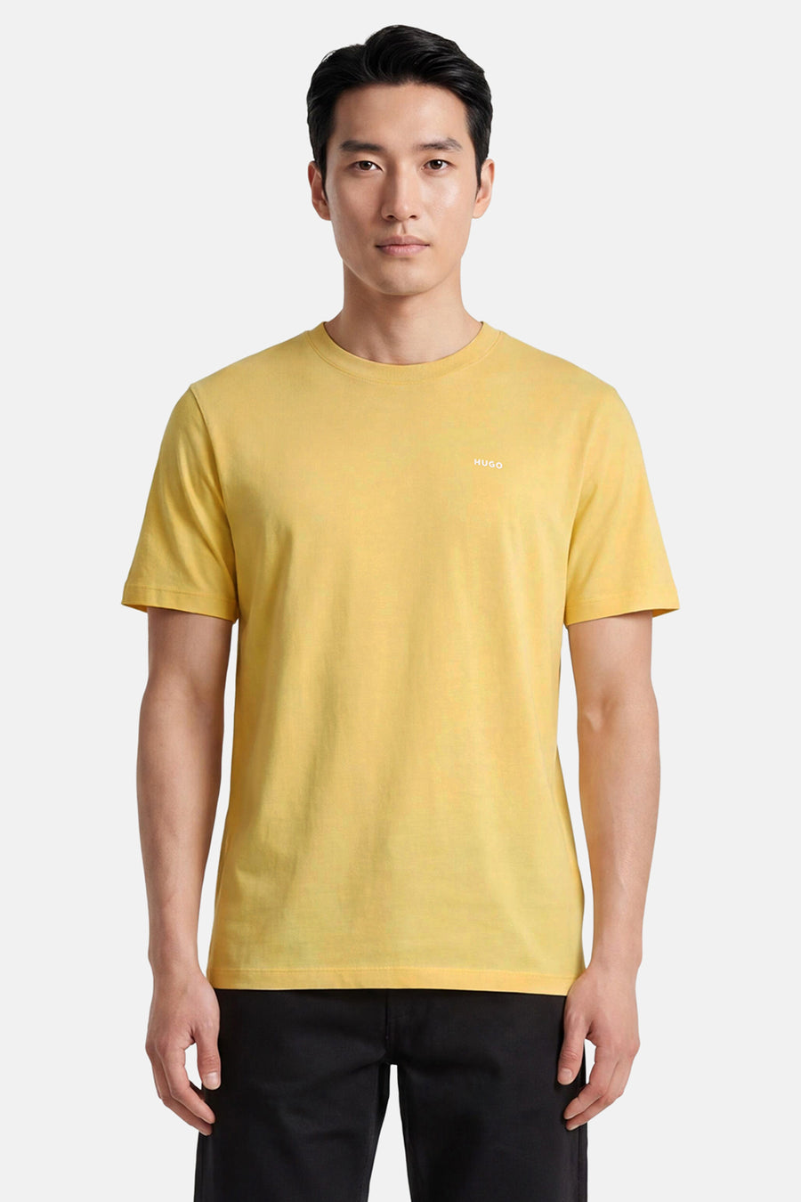 Geel T-shirt met korte mouwen van HUGO, met ronde hals en klein wit logo op de borst, gedragen door een man met zwarte broek.