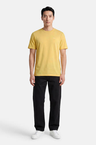 T-shirt jaune à manches courtes de HUGO, avec un petit logo blanc imprimé sur la poitrine, porté par un homme en pantalon noir et baskets blanches.
