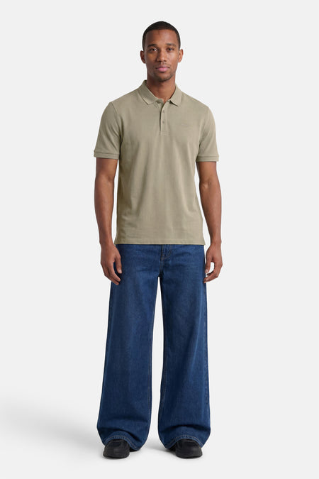 Groene polo van HUGO met logo en korte mouwen, gedragen door een man in een donkerblauwe wide-leg jeans en zwarte sneakers.